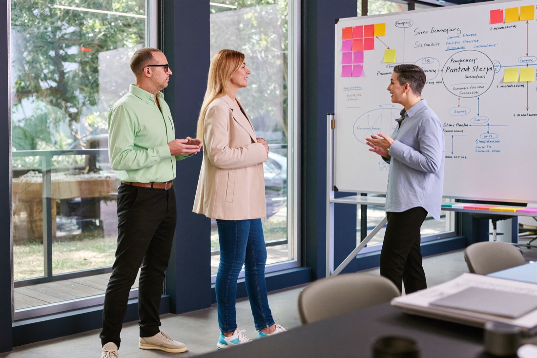Strategie-Workshop: drei Personen besprechen eine Prozessskizze am Whiteboard